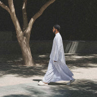 Man in a white outfit walking under a tree at night.